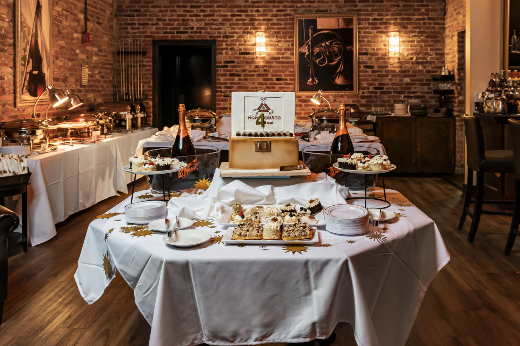 A private-event buffet and dessert display at Red Phone Booth, with a cigar-themed celebration cake and champagne.